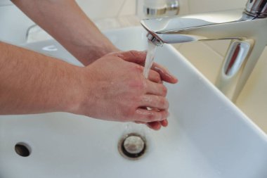 Adam ellerini banyoda yıkıyor. El yıkama. Mikrop yok, sorun yok. Suyun altında ellerini yıkayan adama yaklaş.. 