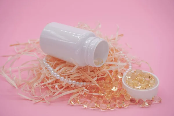 Vitamin pills with bottle on pink background. Yellow medical pills spilling out of bottle.