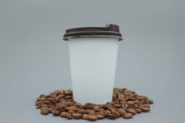 Beyaz kağıt bardak kahve. Kahve çekirdekleri arasında bir kağıt bardak duruyor.. 