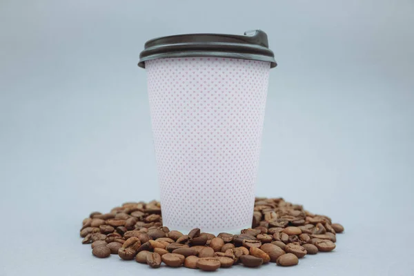 Pink paper cup and plastic lid mockup or mockup, on gray background. Scattered coffee beans.