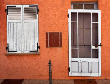 Beyaz ön kapı, kapalı panjurlu beyaz pencereler ve Provence, Fransa 'da eski bir evin turuncu duvarı arasındaki tezat