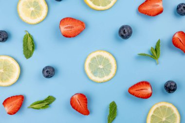 Mavi zemin üzerinde yabanmersini, çilek, limon dilimleri ve nane yaprakları. Sağlıklı beslenme kavramı. Parlak yaz geçmişi, yemek tasarımı. Yüksek kalite 4k görüntü