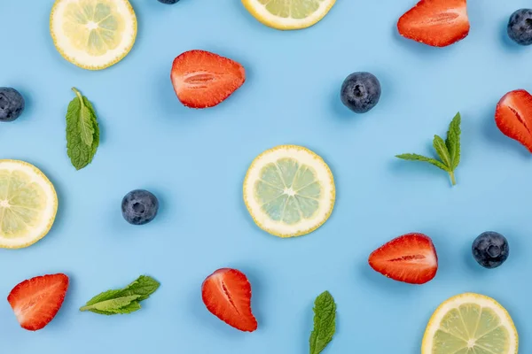 Mavi zemin üzerinde yabanmersini, çilek, limon dilimleri ve nane yaprakları. Sağlıklı beslenme kavramı. Parlak yaz geçmişi, yemek tasarımı. Yüksek kalite 4k görüntü