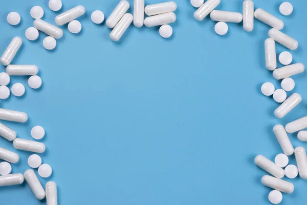 white pills and capsules, medicines on a blue background, the concept of pharmacology, medicine or treatment, a template for inserting text, copy space.