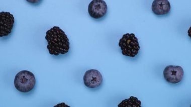Rotating blackberries and blueberries on a blue background, close-up, top view. High quality 4k footage