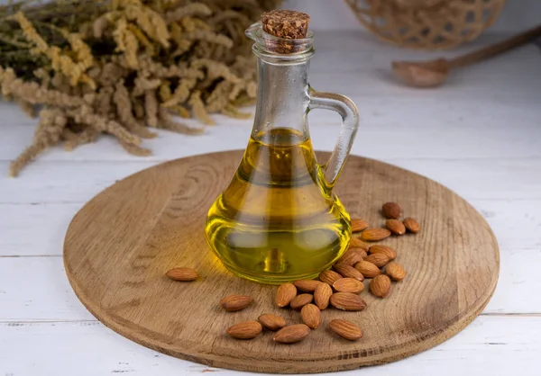 jug or bottle with almond oil on a background of almond nuts on a wooden background.