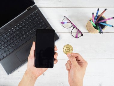 El ele tutuşan cep telefonu ve dizüstü bilgisayarı ve kalem kutusu arkaplan görünümlü altın bitcoin.