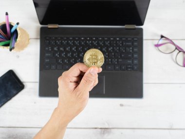Masa üstü çalışma alanındaki dizüstü bilgisayarın klavyesinde el ele tutuşan bitcoin.