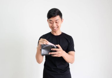 Genç adam siyah gömlekli, gülümseyen ve mutlu hisseden ve cüzdanındaki paraya bakan soyutlanmış zengin adam konseptine bak.