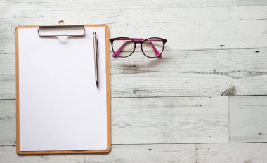 Kağıt üzerinde gümüş kalem tahta pano, beyaz tahta masa üstünde gözlük, uzay gölgesi.