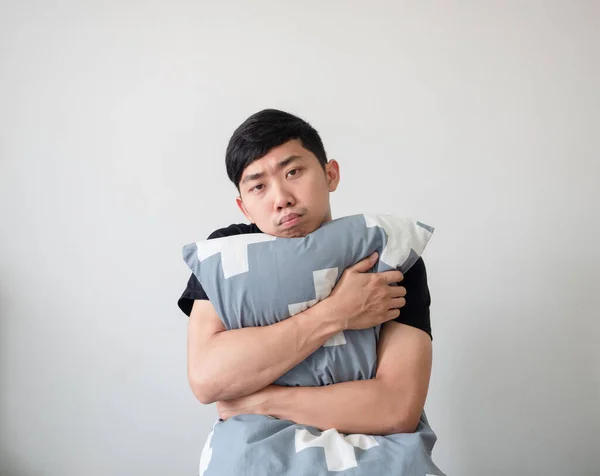 Young man wake up and hugging pillow look at camera bored face on white isolated background
