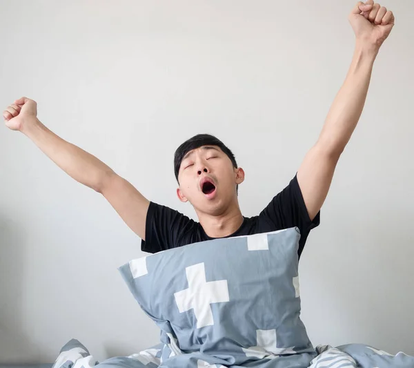 Asian man with pillow wake up at morning and arm up and yawn feel sleepy on white isolated
