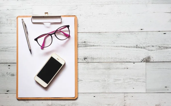 Silver pen and glasses and smartphone on blank white document clipboard on white wood table top view copy space,Business concept