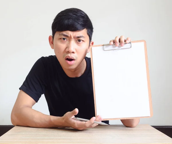 年轻的亚洲人严肃而困惑的脸在剪贴板上显示着白纸坐在办公桌前 上面写着 孤立的白领工作理念 — 图库照片