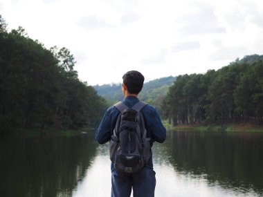 Genç adam sırt çantalı gezgin konsepti vadi ve orman arasında doğal olarak gölün arka planına sahip bir ilham kaynağı arıyor.