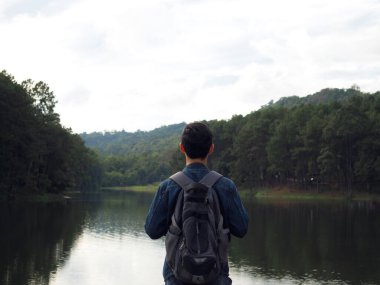 Genç adam sırt çantası gezgini konsepti Göl ve vadi manzarasının önünde