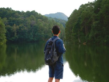 Genç adam sırt çantasıyla gölün ve vadideki arka planda ilham verici bir şekilde duruyor. Turizmci, arkasında dağ bulunan göle ve ormana bakıyor..