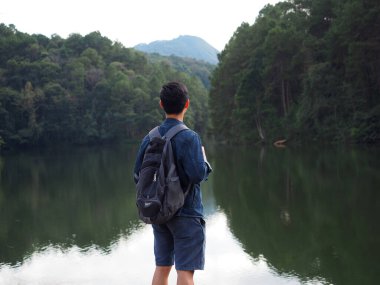 Genç adam, doğal olarak gölün ve vadinin önünde duran sırt çantasıyla gezgin, doğanın arasında gölü olan ormanı ve dağa bakıyor..