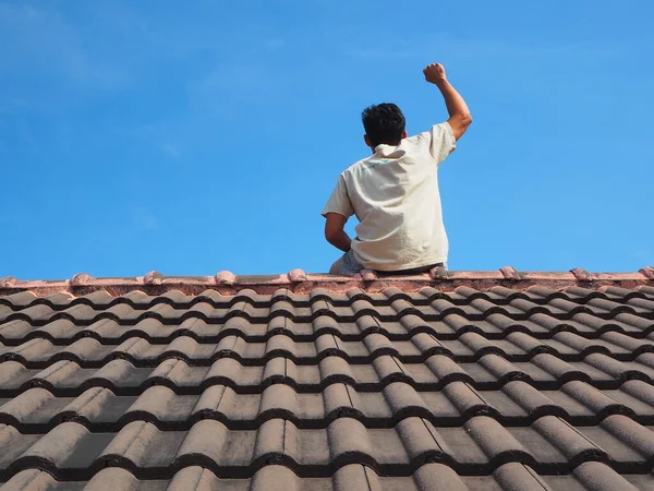 Man sitting on black roof and show hand up with blue sky background and sunshine,Fighting man on the roof