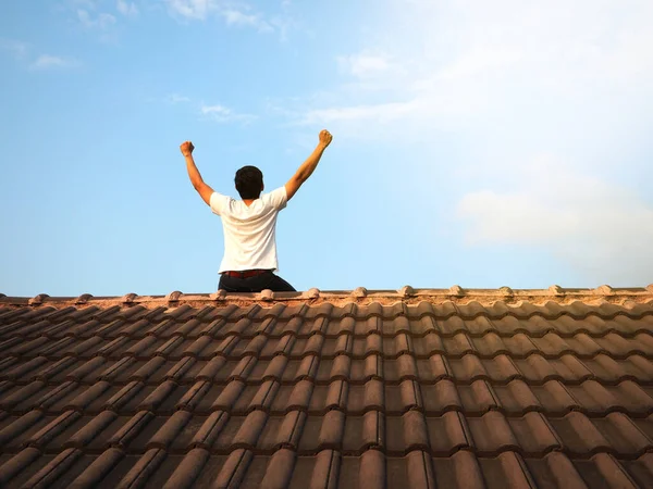 Man sit on the roof with blue sky background success concept,Fighting man sit turn back on black roof and show arm up