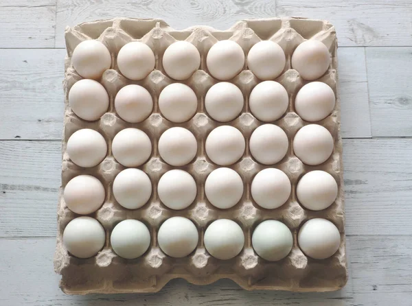 Many duck eggs in carton box on white wood background top view