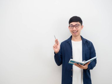 Gözlüklü, neşeli Asyalı genç adam gülümse. Yüzün kalemi kaldırsın ve kitabı elinde tutsun.