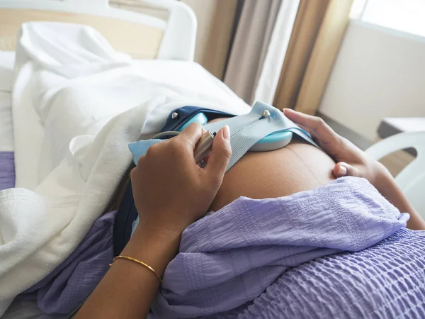 Hastanedeki yatakta bebeği kontrol ettiği için elinde tıbbi düğme olan hamile bir kadın.