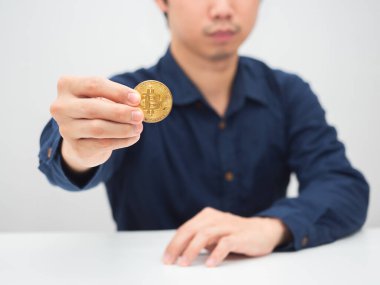 Masada oturan ve elinde altın bitcoin gösteren bir adam.