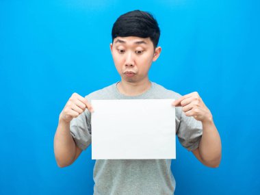 Asyalı adam, mavi arka plandaki boş sayfaya şüpheyle bakıyor.