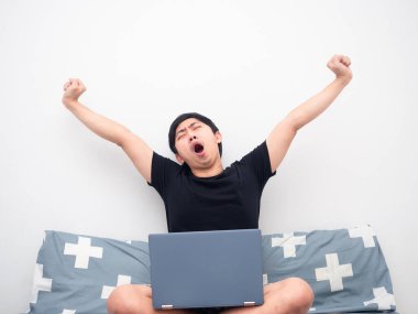 Dizüstü bilgisayarı olan bir adam yatakta uykulu hissediyor.