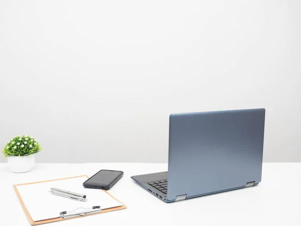 Masa başı iş yerinde beyaz arka planda belge tahtası olan dizüstü bilgisayar