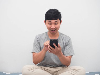 Yatağın üzerinde cep telefonu kullanan genç adam internetten alışveriş yapmaktan zevk alıyor.