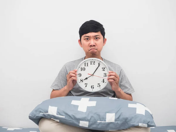 Man sit on the bed holding analog clock angry face,Wake up late concept