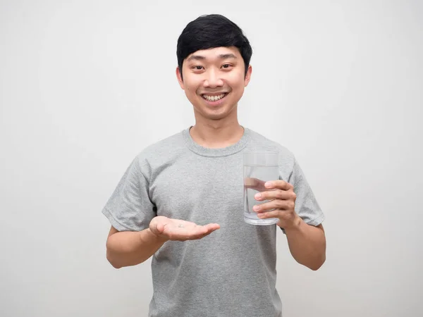 Pozitif genç adam elinde bir bardak suyla nazikçe gülümseyerek ilaç tutuyor.