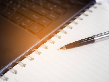 Closeup pen on oage diary with keyboard laptop