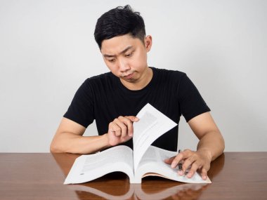 Asyalı adam masada ciddi ciddi ders kitabı okuyor.
