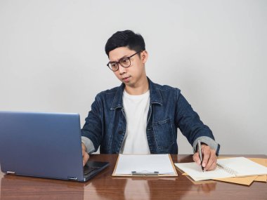 Young businessman jeans shirt sit and writing and using laptop at his workplace table