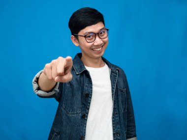 Asian man jeans shirt gesture point finger at you blue background