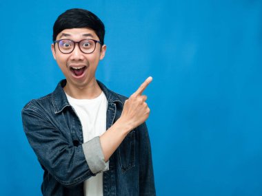Positive man jeans shirt gesture point finger at copy space blue background