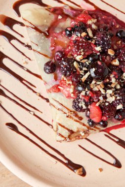 photo of delicious crepe with red berries, blackberries, blueberries, blueberries, strawberries and chocolate decoration. sweet crepe.