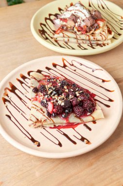 photo of delicious crepe with red berries, blackberries, blueberries, blueberries, strawberries and chocolate decoration. sweet crepe.