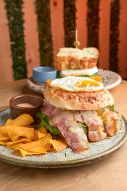 photo of delicious bacon burger accompanied with an egg, chipotle dressing and dehydrated bananas on wooden table. big hamburguer. accompanied with a panela sandwich