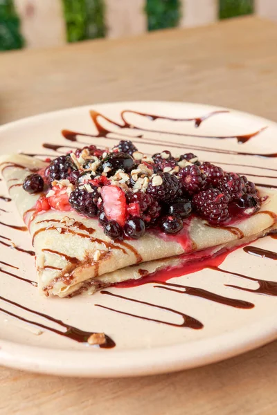 photo of delicious crepe with red berries, blackberries, blueberries, blueberries, strawberries and chocolate decoration. sweet crepe.