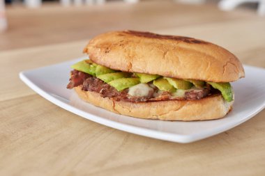 picture of delicious sandwich or Torta with meat, avocado and cheese on wooden table.. typical mexican food.