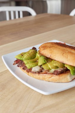 picture of delicious sandwich or Torta with meat, avocado and cheese on wooden table.. typical mexican food.