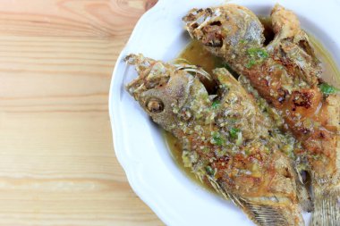 Tayland Devi gourami balığı ve sarımsak. Çam ağacından masada, beyaz tabakta kızartılmış tatlı ve baharatlı sos. Tatlı biberli kızarmış balık. Baharatlı soslu Tayland yemeği. Tayland tarzı yemek..