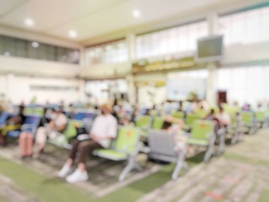 Chiang Rai uluslararası havaalanındaki kahve dükkanının yanında bekleyen insanların ya da yolcuların bulanık görüntüleri. Bagajı olan gezgin koltukta oturuyor ve uzun kuyruk halindeki bokeh ışığıyla dolu.