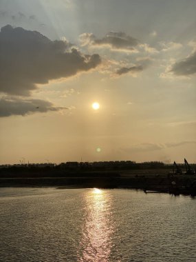 Ufukta göl olan bir gün batımı manzarası. Güneş ışınları ve yansımalarıyla gökyüzüne,.