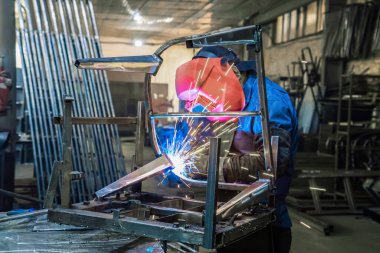 Üretimde olan bir kaynakçı ürün imalatında çalışmaktadır. Maskeyle, eldivenlerle, kıvılcımlar uçuşuyor