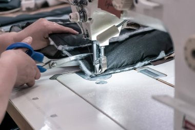 A seamstress cuts fabric while working at a sewing machine in the workshop. Women's hands